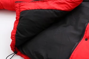 Détail d'une veste d'hiver rouge montrant fermeture éclair, bouton pression et cordon de serrage