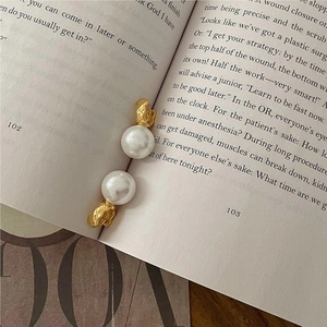 Detail of elegant gold pearl earrings with quilted texture on a vintage book page