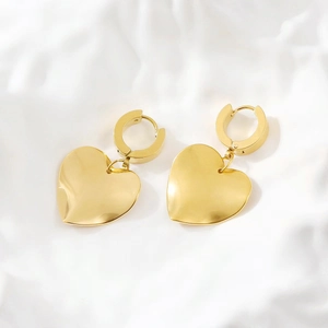 Close-up of golden stainless steel heart-shaped earrings on elegant white silk background