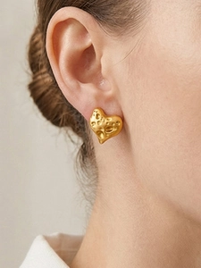 Nahaufnahme von gehämmertem 18k Gold Herzohrring am Ohr eines Models getragen