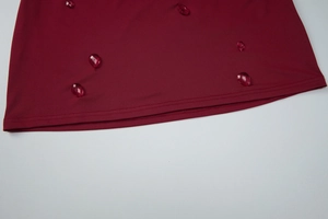 Detail of red teardrop rhinestones on the stitched hem of a dark red knit dress