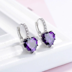 Macro shot of purple heart-shaped zircon earrings with silver setting on white prop