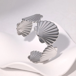 Silver stainless steel scallop shell cuff bracelet on a white textured wave pedestal