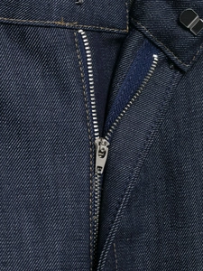 Dettaglio della cerniera metallica e del bottone sui jeans a botte in denim blu scuro