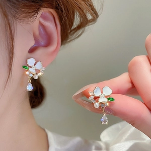 Detailed view of floral earring with white enamel petals, pearls and drop crystal