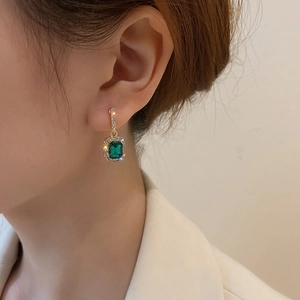 Close-up of geometric green gemstone earrings with white diamonds on model's ear