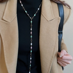Close-up of a long Y-shaped necklace with colorful resin stones worn over a black sweater
