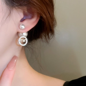 Detail of pearl earrings with zircon letters and dual-wear structure on a model