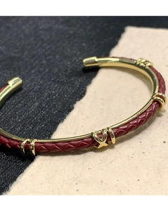 Dettaglio macro del bracciale in pelle intrecciata rossa con accento a X dorato lucido