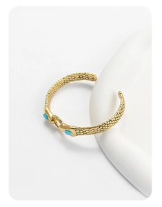 Detail of snake head with blue gemstone eyes and textured scales on gold-tone cuff