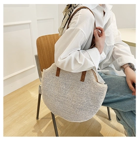 Detail of handwoven straw tote with brown leather handles and reinforced stitching for beach