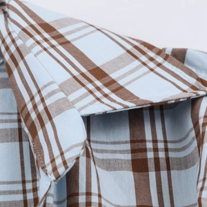 Detailed view of plaid poplin fabric texture and shoulder seams on a blue checkered shirt