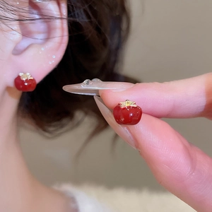 Macro shot of tomato stud earrings with red enamel finish and golden leaf details