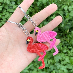 Detail of handmade beaded flamingo keychains in red and pink with green plant background