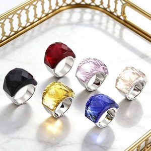 Set of six colorful faceted crystal rings on a gold tray over white marble base