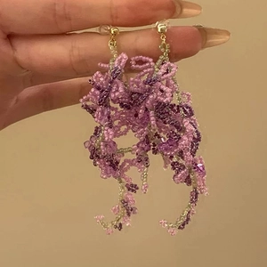 Detail of handcrafted purple and green bead earrings with delicate floral woven pattern