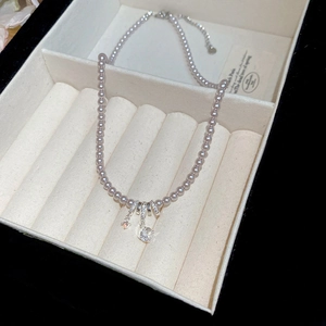 Gros plan du collier de perles avec pendentif triple anneau serti sur support velours