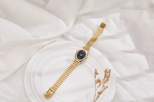 Elegant gold oval watch with black dial placed on a white porcelain dish with dried flowers