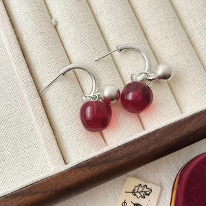 Elegant red cherry pendant earrings with silver needles on a beige velvet jewelry tray