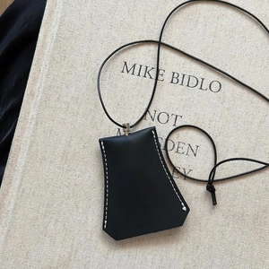 Detailed view of black trapezoid faux leather glasses holder with white contrast stitching