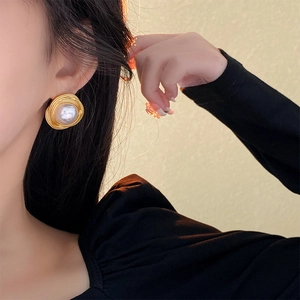 Close-up of vintage gold irregular metal earrings with large white pearls on a model