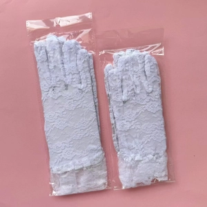 Close-up of white floral lace gloves with ruffled wrist detail in protective packaging