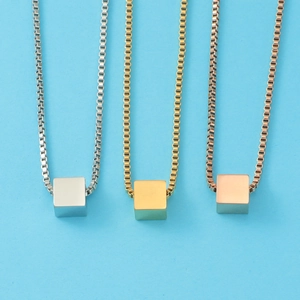 Three square cube pendant necklaces in silver, gold, and rose gold on light blue background