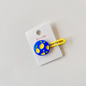 Detail of yellow wavy metal hair clip with blue floral charm on card display