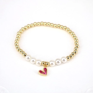 Detailed close-up of a gold beaded bracelet with pearls and a red zircon heart charm