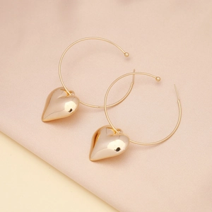 Close-up of golden 3D heart-shaped pendant earrings on soft draped fabric