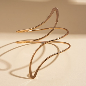 Detailed view of polished golden irregular leaf spiral arm cuff on a minimalist background