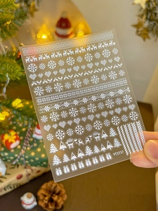 Macro shot of white snowflake and reindeer nail art decals on a model hand with festive decor