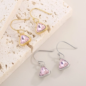 Detailed view of gold and silver triangle pink crystal earrings on textured stone
