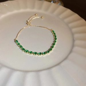 Elegant gold adjustable bracelet featuring sparkling green oval-cut stones on a white tray