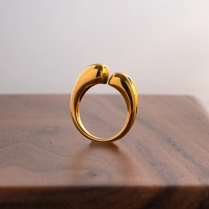 Polished gold teardrop open ring in stainless steel displayed on a wooden stand