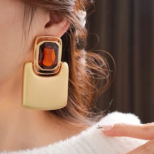 Close-up of matte gold rectangle earrings featuring a large orange gemstone on a model