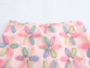 Detailansicht von 3D-Netzblumen-Applikationen mit bunten Pailletten auf einem rosa Rock