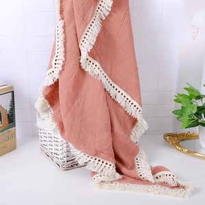 Detail of pink cotton muslin baby blanket with decorative white lace tassel fringe