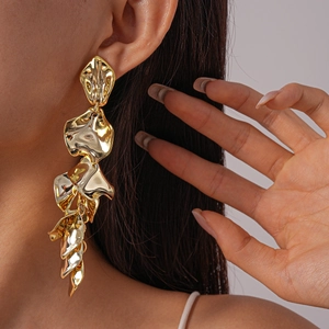 Detailed close-up of long layered golden leaf earrings worn by a model on a grey background