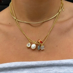 Close-up of layered gold necklaces with colorful zircon pendants and pearls on a model