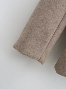 Gros plan détaillé sur la texture épaisse du tissu en laine et le poignet du manteau beige