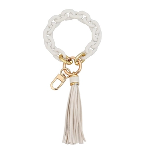 Macro shot of white matte chain keychain with golden clasp and beige suede tassel