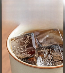 Macro detail of Ru ware ceramic tea cup with reddish-brown rim and ice cubes
