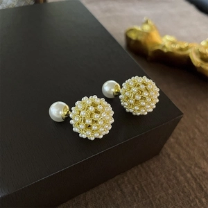 Macro detail of gold-plated mesh earrings with cluster faux pearls on a black base