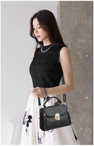 Detail view of black leather handbag with golden metal clasp and adjustable shoulder strap