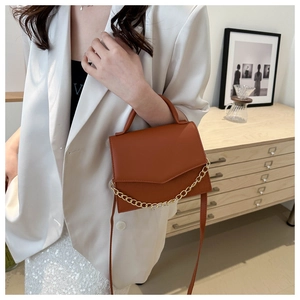 Detail of a brown leather crossbody bag featuring a decorative gold chain on a model