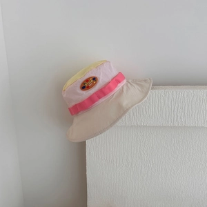 Detail of pink and yellow kids sun hat with leather label on textured white background