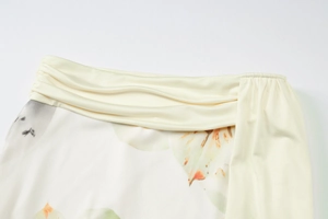 Detailed view of cream-colored pleated waistline and elegant floral print on mesh dress