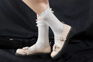 Détail de chaussures Mary Jane beige avec boucle cœur et volants sur fond noir