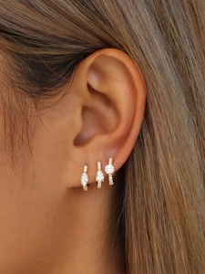 Detailed view of three gold-plated huggie earrings with marquise and round zirconias
